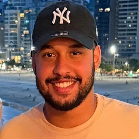 Foto de perfil de Eitor Barbarote, sorrindo de boné à noite na orla